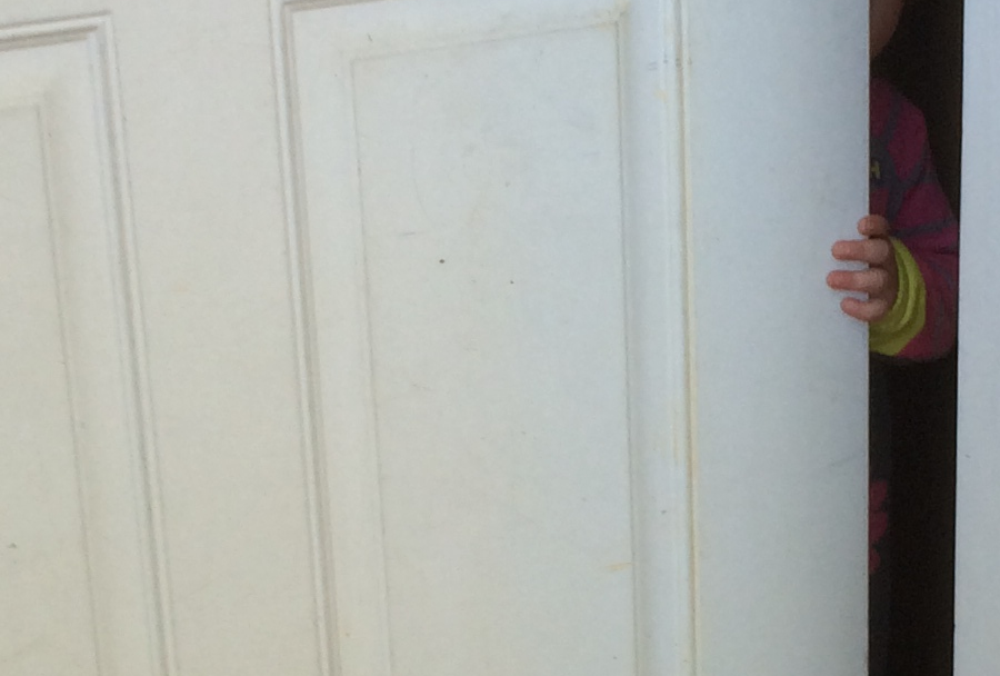 a child's hand holding the edge of a slightly open door